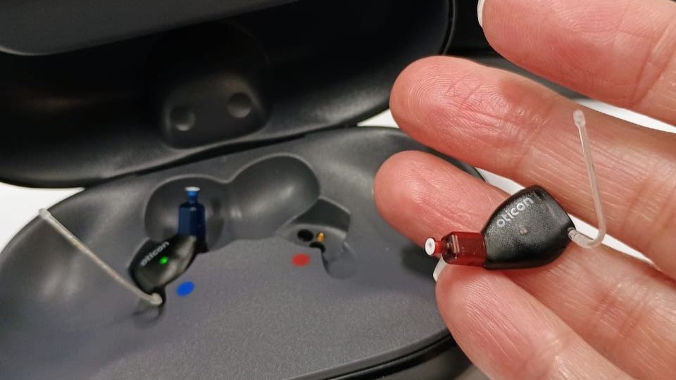 A hand holding the new Oticon Intent™ smart hearing aid over its sleek black recharging case at Newmarket Hearing Clinic.